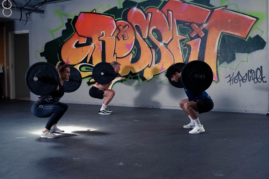 En kvinde og to mnd i et fitnesscenter laver squat med en stang p ryggen,