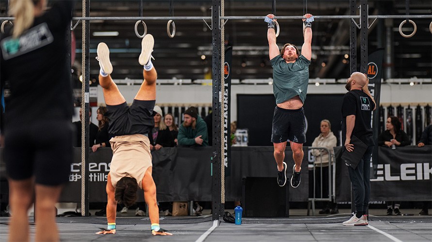 Billede af to mnd, der trner CrossFit, en p hnderne og en hngende i ringe.