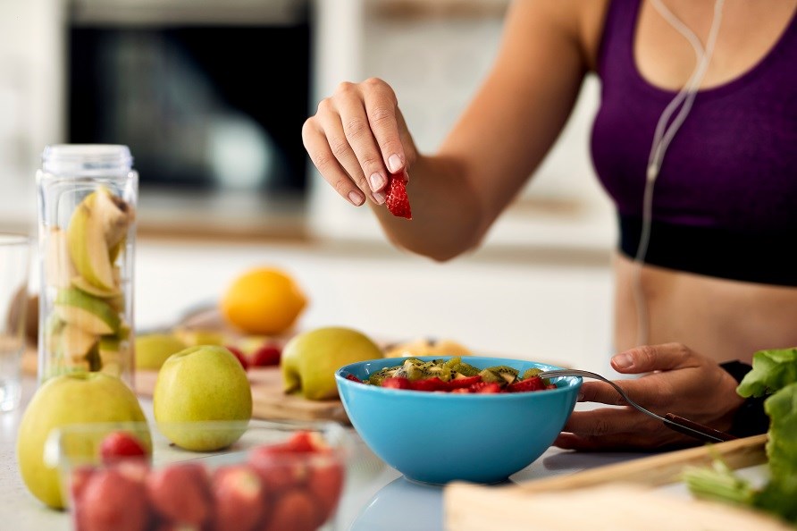 En kvinde er ved at lave en smoothie bowl med frugt som topping.