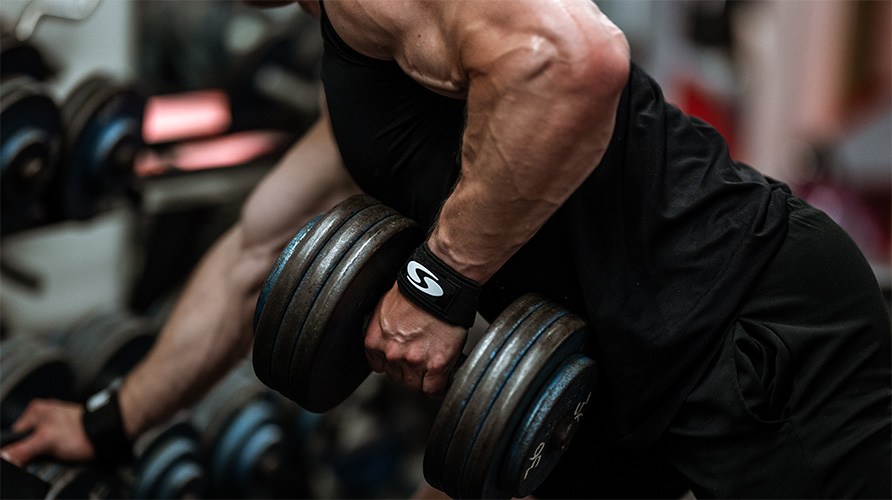 En muskuløs mand laver en-armetroning med en håndvægt i et træningscenter. En muskuløs mand laver en-armetroning med en håndvægt i et træningscenter.