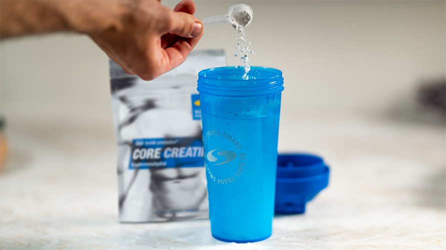 En h�nd h�lder en skefuld Core Creatine i en bl� shaker.