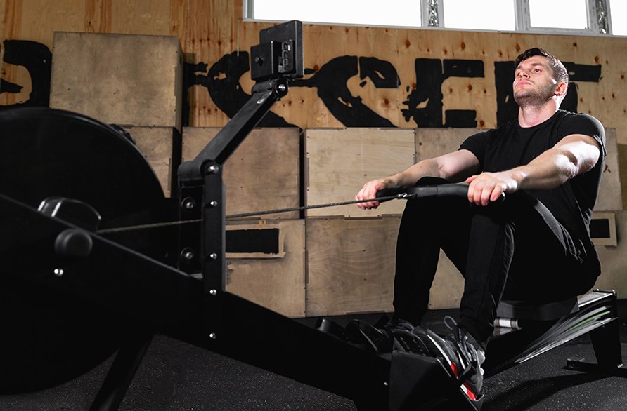 En mand sidder i en romaskine og tr�ner, i et tr�ningscenter.