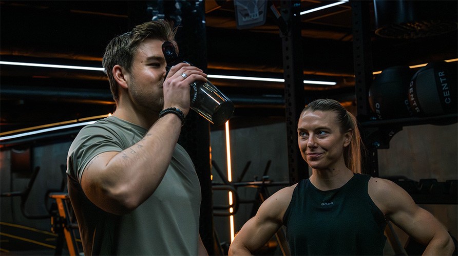 Kvinde og mand i et tr�ningscenter, manden drikker en proteinshake.