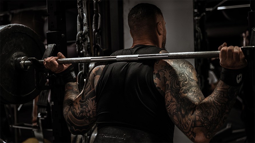 En mand med muskul�s ryg st�r ved en v�gtstang.