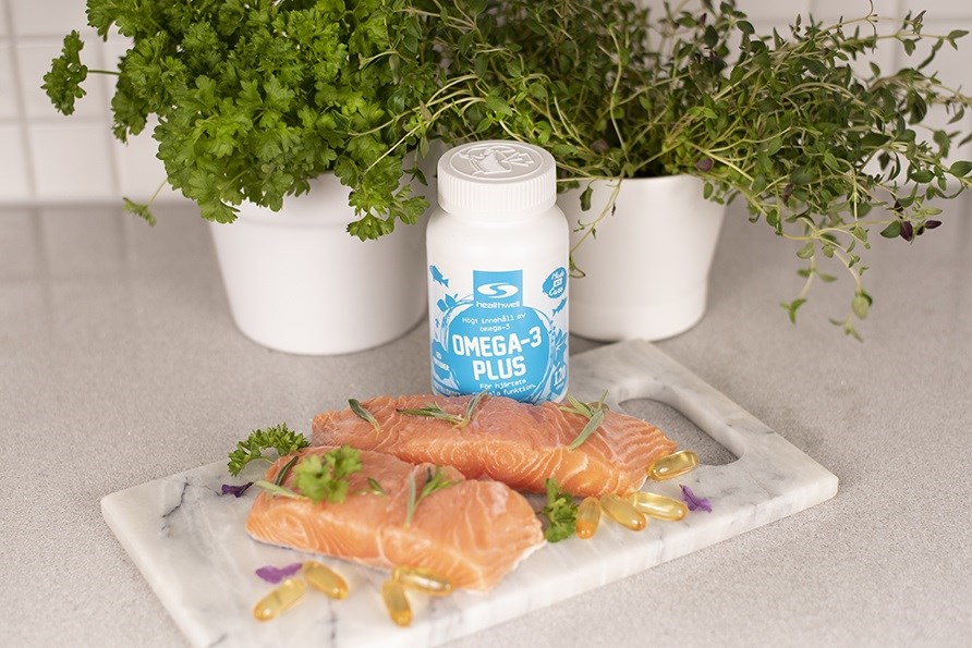 To friske laksesteaks p en marmorskrebrt med omega-3 kapsler ved siden af og en btte Omega-3 Plus fra Healthwell.