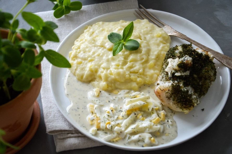 En hvid tallerken med torsk, kartoffelmos og ggesauce, klar til servering.