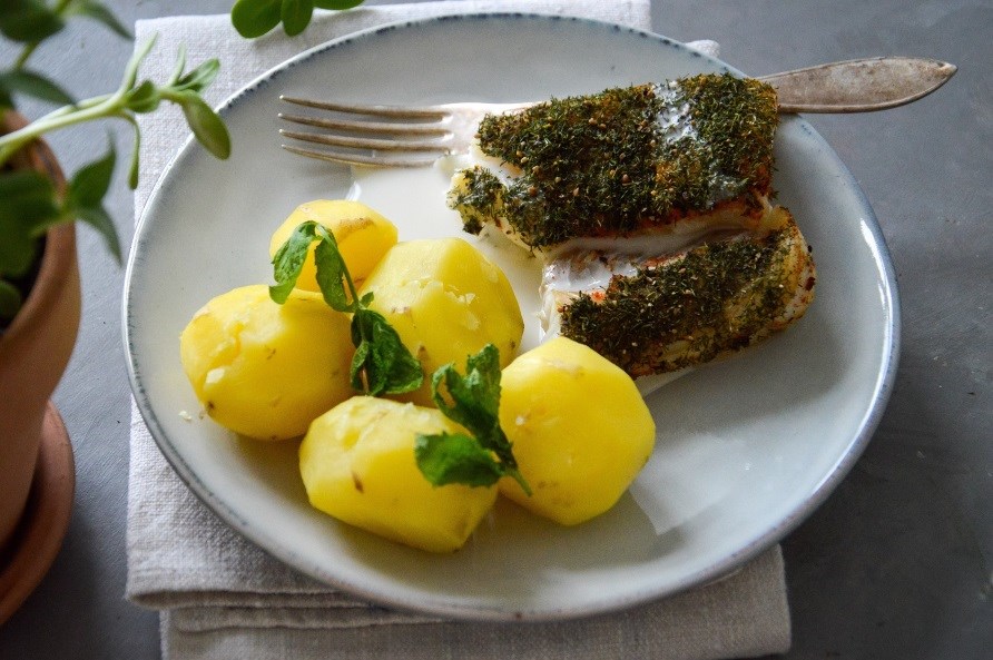 En portion torsk med peberrodssauce og kogte kartofler p en tallerken.