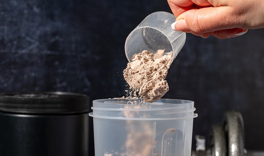 En hånd hælder kasein pulver i en shaker. En hånd hælder kasein pulver i en shaker.
