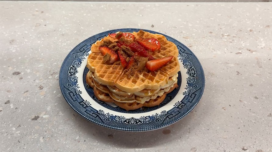 Proteinrige vafler ligger p� en tallerken, toppet med jordb�r, sirup og brun farin.